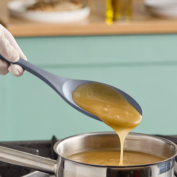 A person using a Tablecraft solid silicone spoon to pour liquid onto a pan.