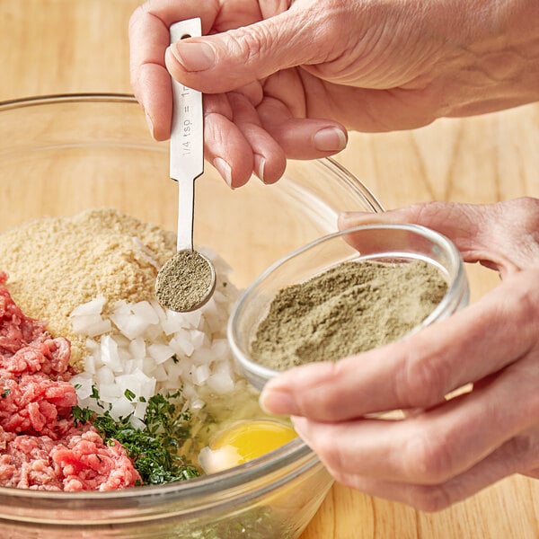 A person adding Regal Ground Marjoram to a bowl of meat.