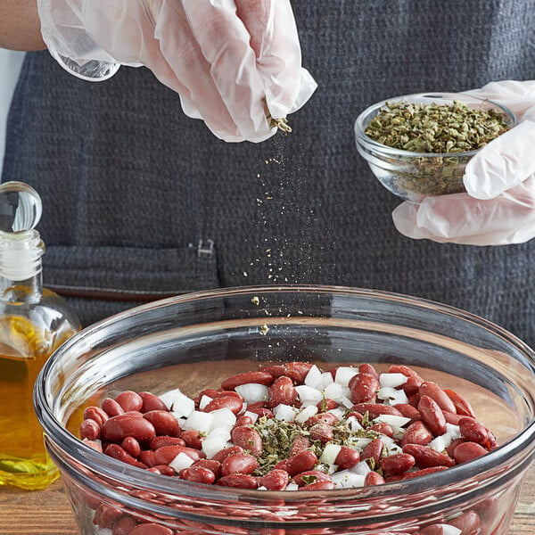 A person pouring Regal Mexican Oregano leaves into a bowl of red beans.