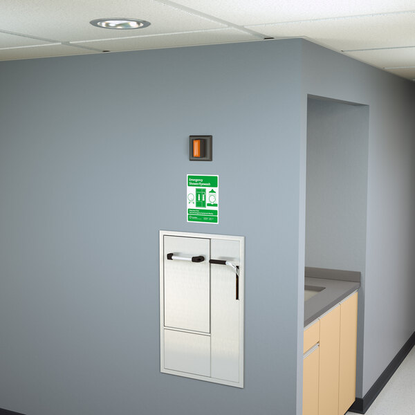 A wall with a white Guardian Equipment Recessed Safety Station and a sign above a metal door.