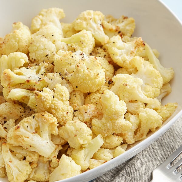 A bowl of cauliflower with a spoon and fork on a white background.