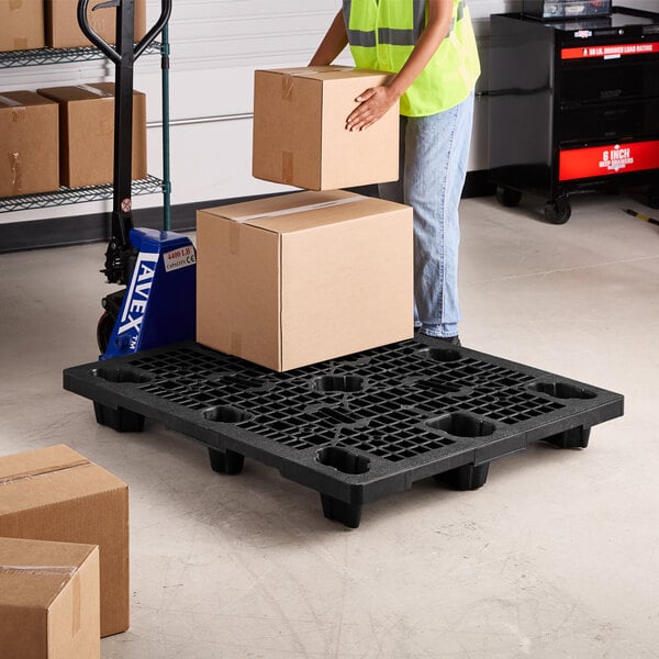 A woman holding a box standing on a black plastic pallet.