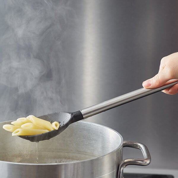 A hand using a Tablecraft slotted spoon to stir pasta in a pot.