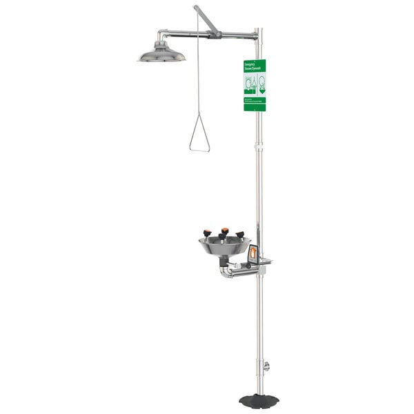 A close-up of a polished chrome Guardian Equipment safety station with a green sign above a shower head.