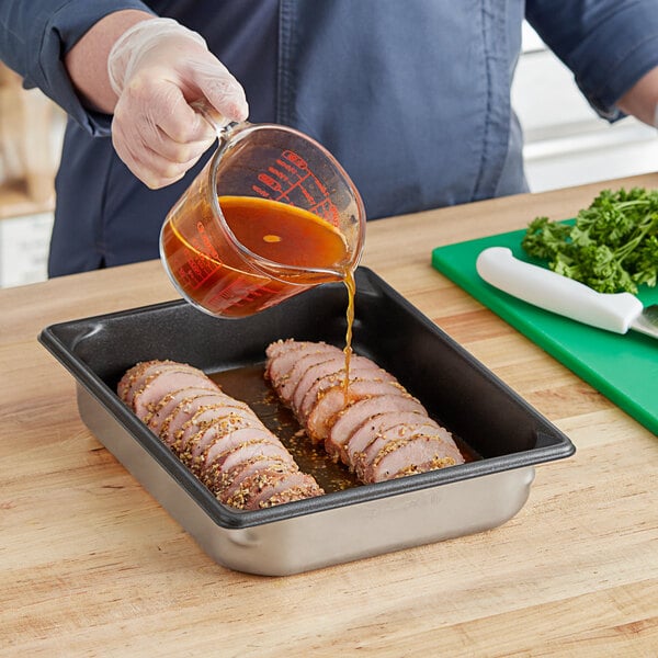 A person pouring sauce into a stainless steel Vollrath steam table pan of meat.