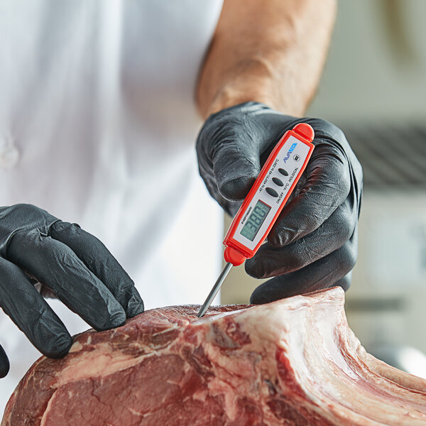 A digital pocket probe thermometer with a red casing being used to measure the temperature of raw meat.