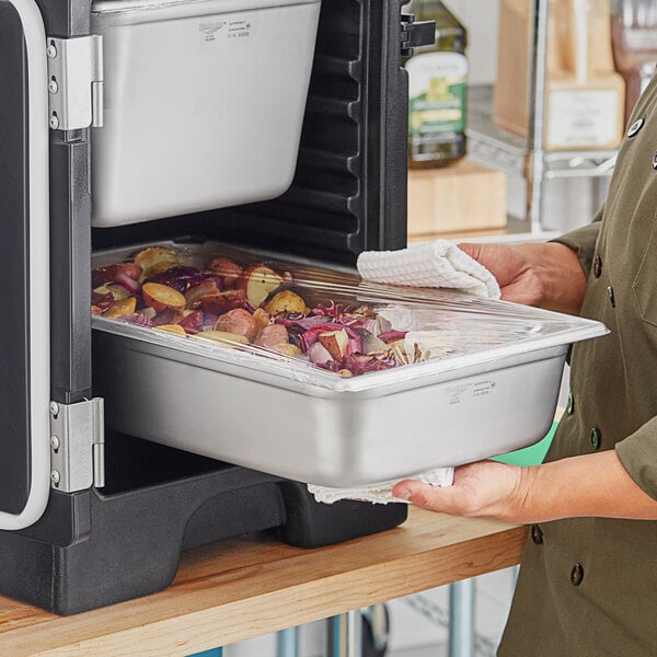 A woman carrying a tray of food in a Vollrath stainless steel transport pan.