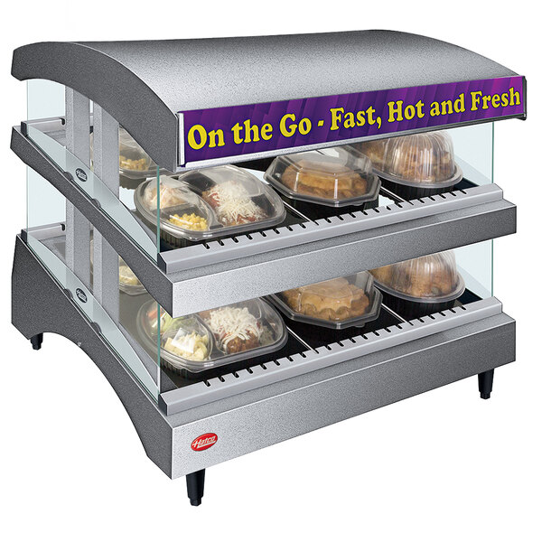 A Hatco Gray Glo-Ray heated glass merchandising warmer with food trays on double shelves in a display case.