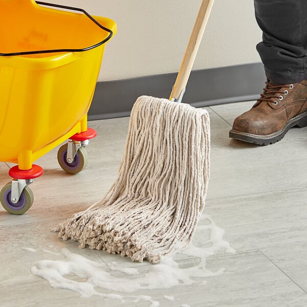 A person using a Choice Natural Cotton Cut End Wet Mop to clean the floor in a yellow bucket on wheels.