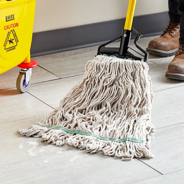 A person using a Choice Natural Cotton Looped End Wet Mop to clean a floor in a room with a yellow caution sign.