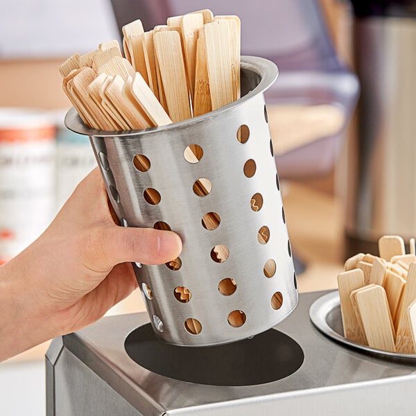 A hand holding a Tablecraft stainless steel cylinder filled with wooden sticks.