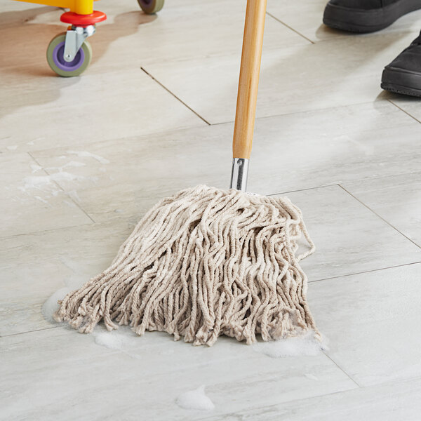 A person using a Lavex Natural Cotton wet mop to clean a floor.