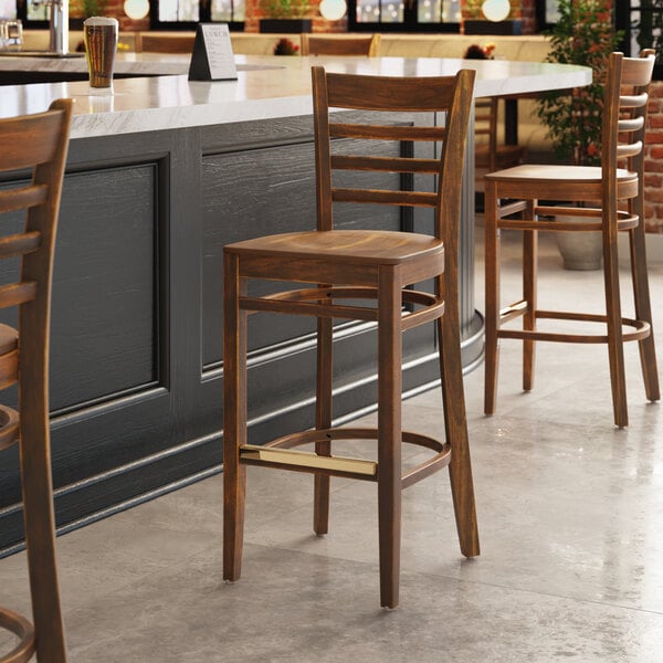A Lancaster Table & Seating vintage wood bar stool with a vintage wood seat at a table in a pub.