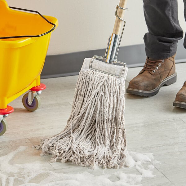 A person cleaning a floor with a Choice Natural Cotton Cut End Wet Mop in a yellow bucket.