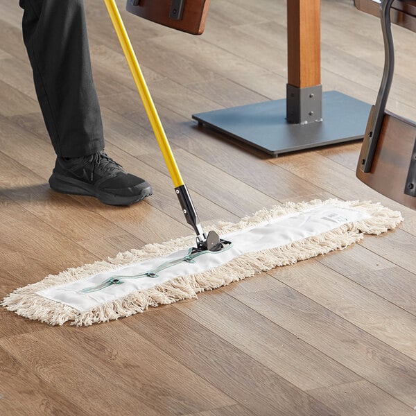 A person using a yellow-handled Choice Natural Cotton dry mop to clean a floor.