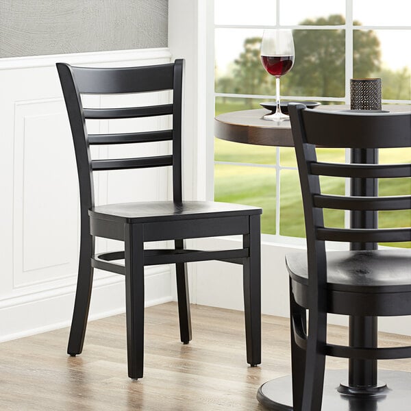 A Lancaster Table & Seating black wood ladder back chair with black wood seat on a table in a restaurant dining area.