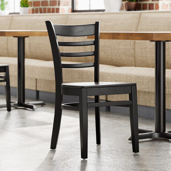 A Lancaster Table & Seating black wood ladder back chair with a black wood seat next to a table in a restaurant.