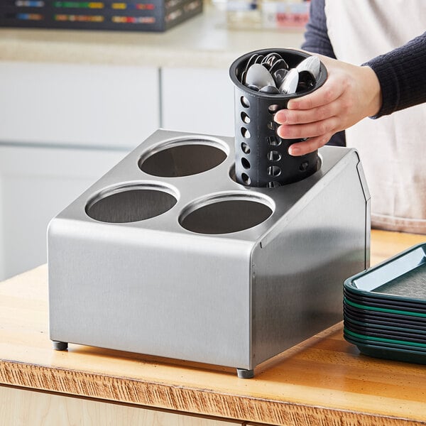 A hand putting spoons in a Tablecraft stainless steel cylinder holder.