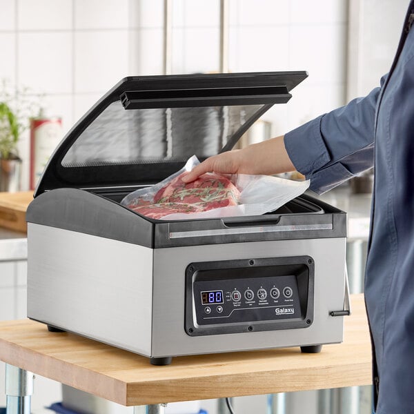 A chamber vacuum packing machine with a digital control panel and a 12-inch seal bar, shown sealing a bag of meat.