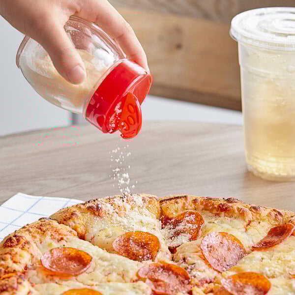A person using a Tablecraft clear glass shaker with red plastic flip top to sprinkle cheese on a pizza.