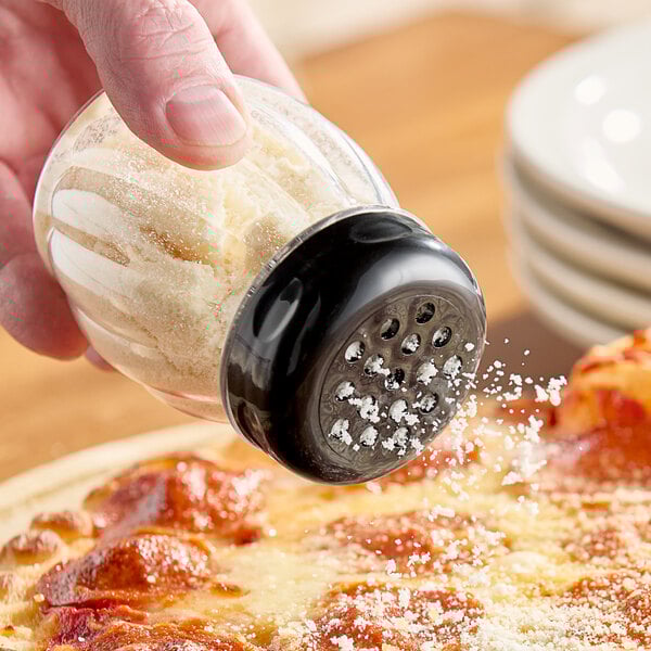 A person using a Tablecraft clear plastic shaker to sprinkle salt on a pizza.