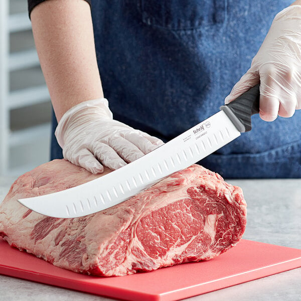 A person in gloves using a Schraf cimeter knife to cut raw meat on a cutting board.