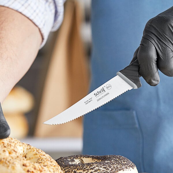 A person in black gloves using a Schraf serrated utility knife to cut a bagel.