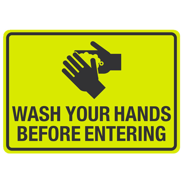 A yellow sign with black text and hands washing that says "Wash Your Hands Before Entering"