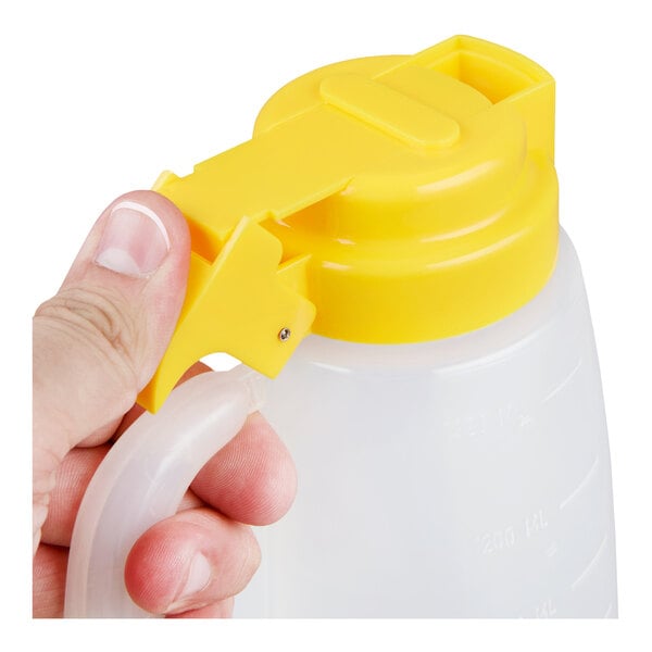 A plastic dispenser jar with a yellow lid and handle, being held by a hand.