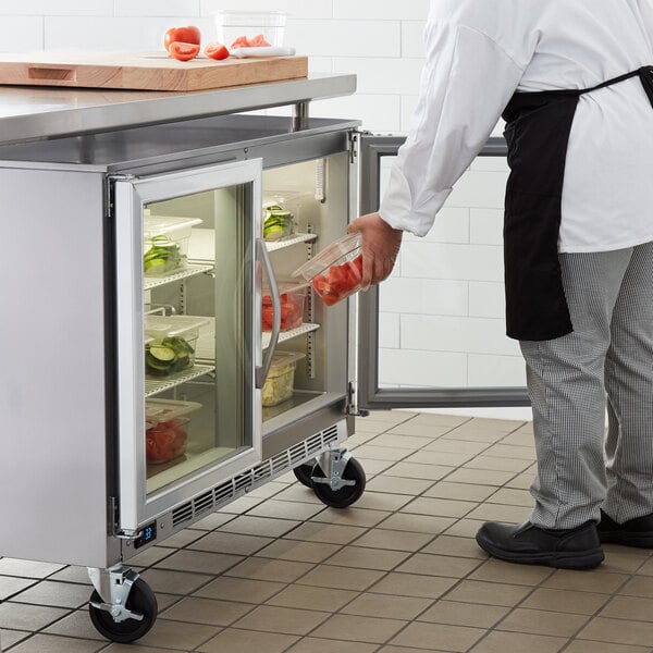 A person putting food into a Beverage-Air undercounter refrigerator with glass doors.