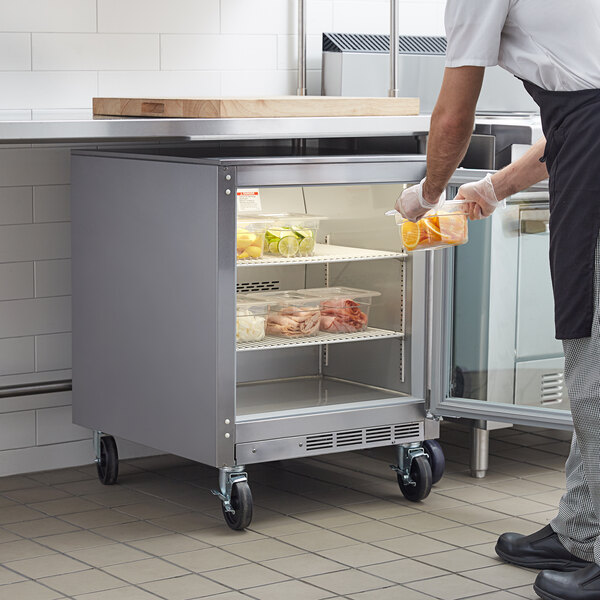 A man in a white apron putting food into a Beverage-Air undercounter refrigerator.