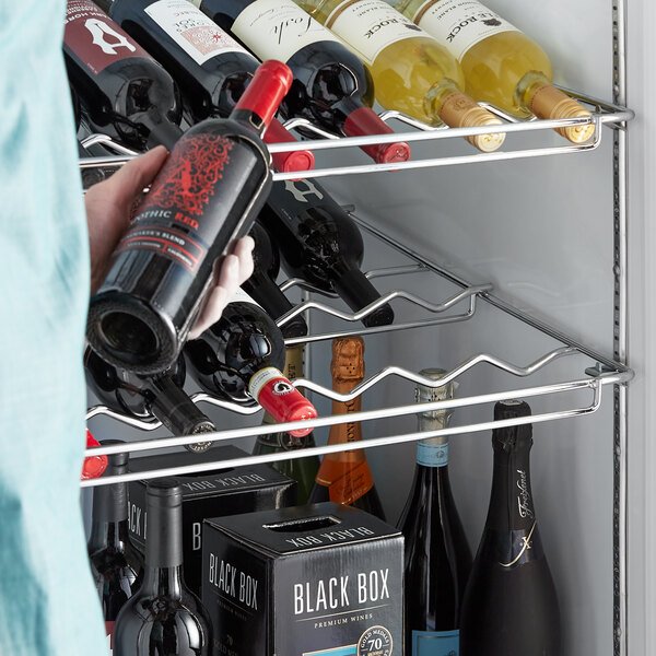 A person holding a bottle of wine in a white curved metal wine rack.