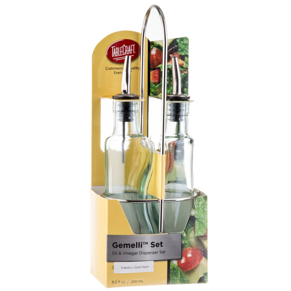 A Tablecraft Gemelli clear glass oil and vinegar cruet set on a counter in a stainless steel rack.