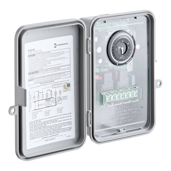 An electric timer device with a dial and wiring terminals, housed in a gray protective enclosure.