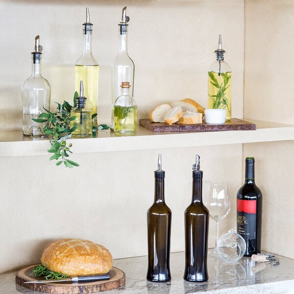 A shelf with Tablecraft dark green glass oil and vinegar bottles filled with yellow liquid.