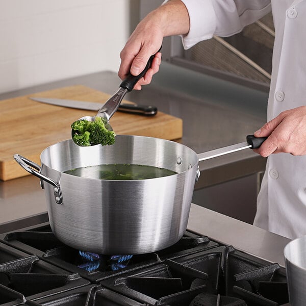 A person stirring broccoli in a Choice sauce pan on a stove.