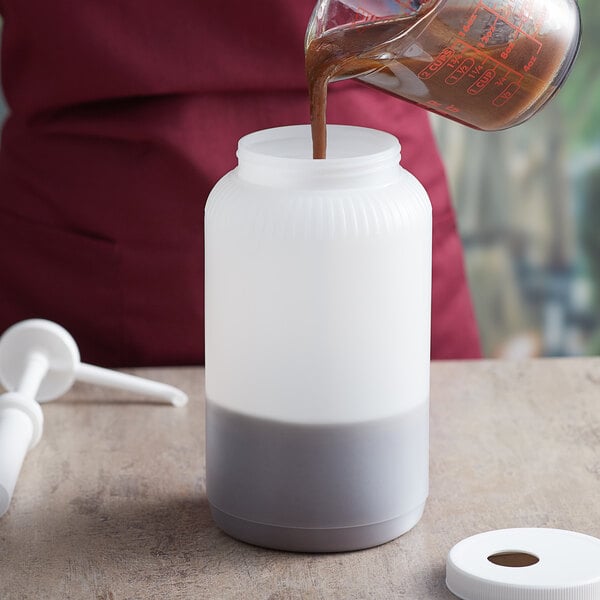 A person pouring brown liquid into a Tablecraft white container.