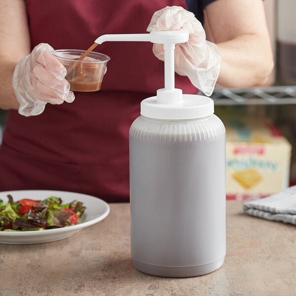 A woman using a Tablecraft condiment pump to pour brown sauce into a plastic container.