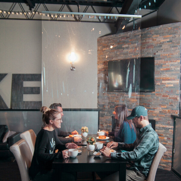 A group of people sitting at a table with a Goff's Clear PVC Hanging Partition overhead.