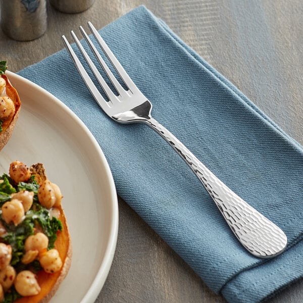 An Acopa Industry stainless steel dinner fork on a napkin next to a plate of food.