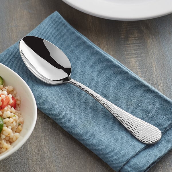 An Acopa stainless steel serving spoon on a napkin next to a bowl of food.