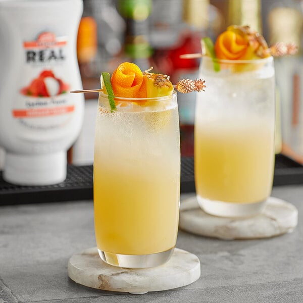 Two glasses of yellow liquid with orange slices and garnish on a table in a cocktail bar.