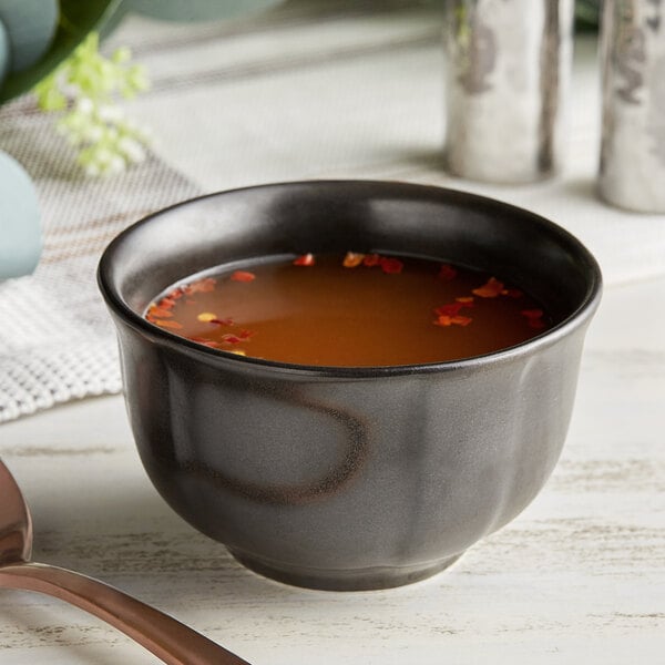 An Acopa Armor Gray scalloped porcelain bouillon cup filled with brown soup and a spoon.