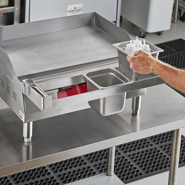 A man holding a Universal 24" Griddle Condiment Rail on a stainless steel counter.
