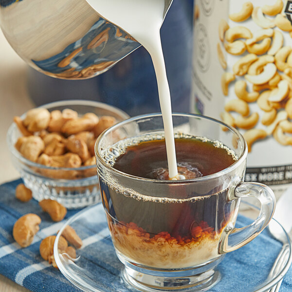 A glass cup of Elmhurst Milked Cashews being poured into a cup of coffee.