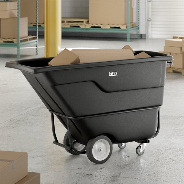 A black Lavex standard-duty tilt truck or trash cart with a 1 cubic yard capacity, shown holding cardboard boxes in a warehouse setting.