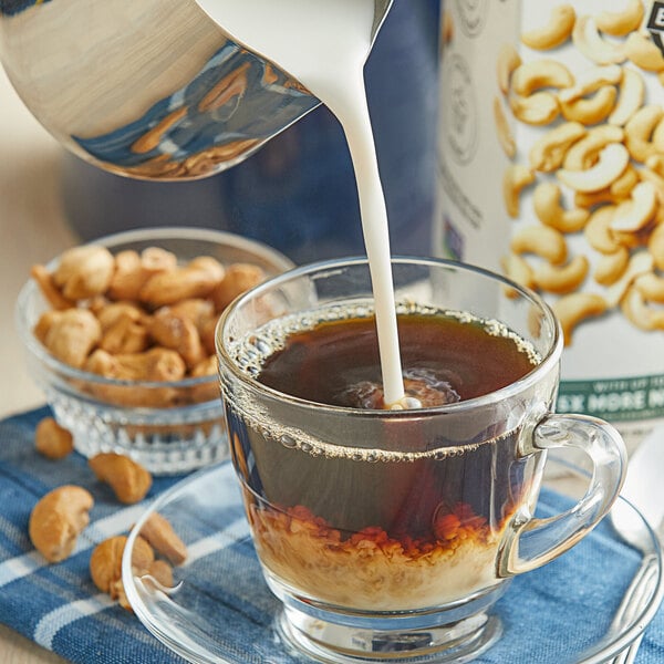 A glass cup of coffee with Elmhurst Unsweetened Milked Cashews pouring into it.