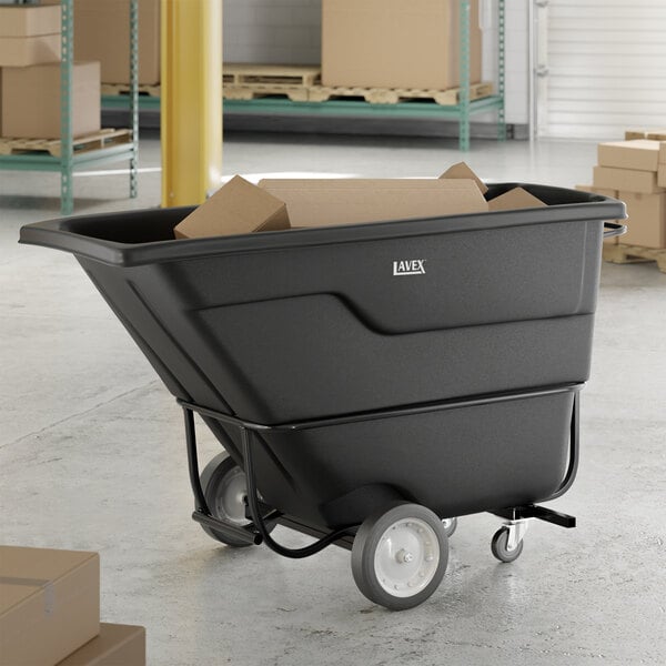 A black forkliftable tilt truck or trash cart with a 1 cubic yard capacity, shown holding cardboard boxes in a warehouse setting.