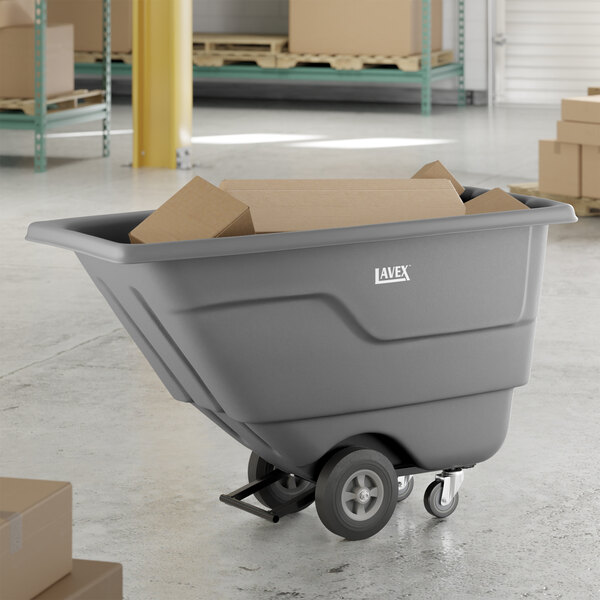 A gray tilt truck or trash cart with a 0.5 cubic yard capacity, holding cardboard boxes in a warehouse setting.