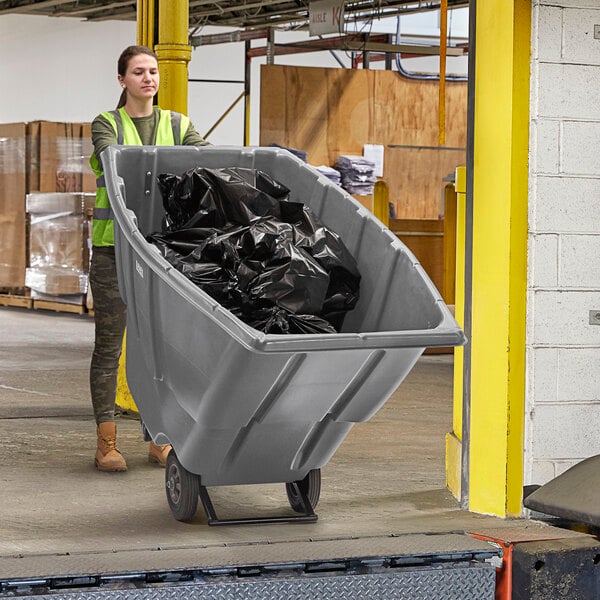 A woman in a yellow vest pushing a Lavex grey light-duty tilt trash cart.